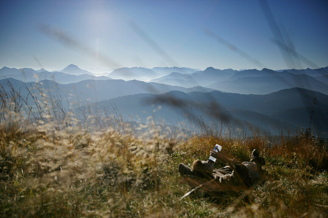 Man lying in the grass, having a break, ridge of Benediktenwand, Karwendel mountains in the background, Bavaria, Germany