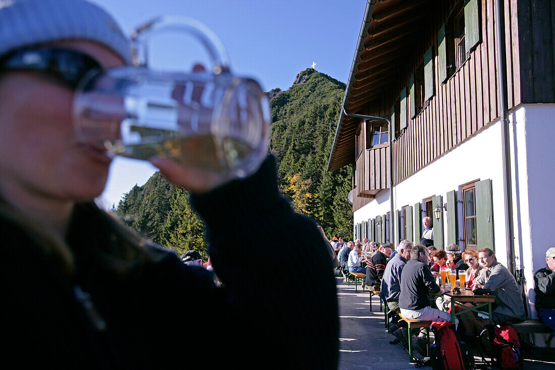 Frau genießt ein Bier am Herzogstandhaus, Martinskopf im Hintergrund, Bayern, Deutschland