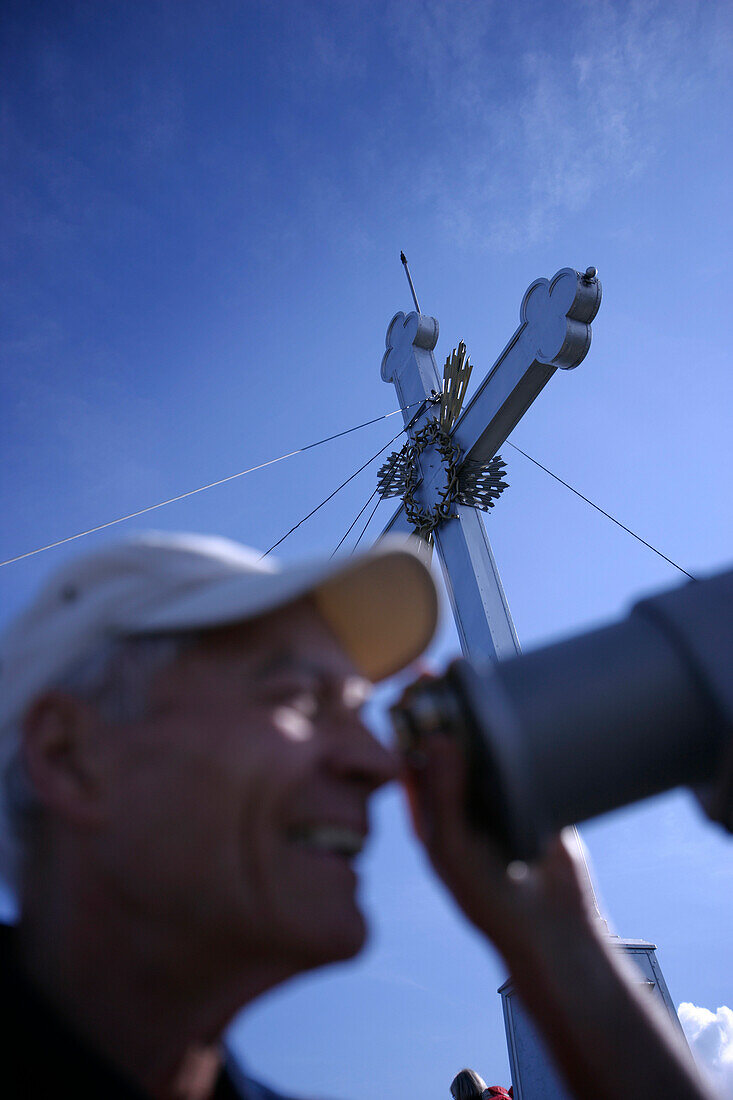 Close up of a man looking through a telescope at the summit cross, Wallberg, Tegernsee, Bavaria, Germany