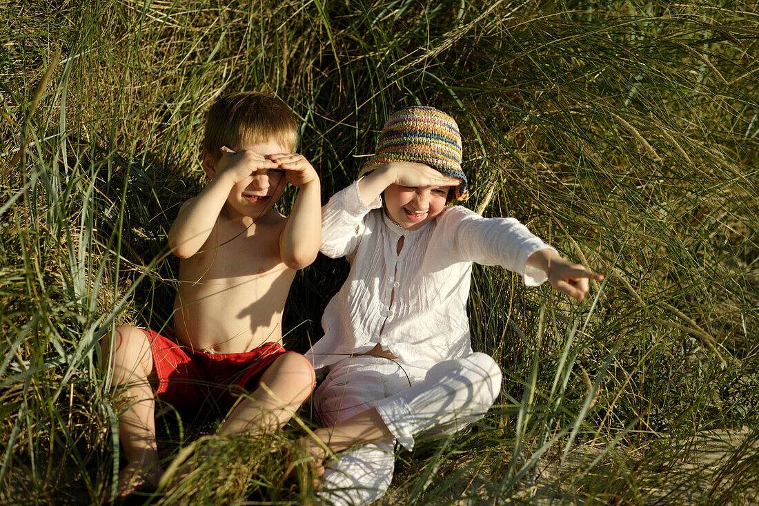 Mädchen und Junge sitzen im Dünengras, Travemünder Bucht, Schleswig-Holstein, Deutschland