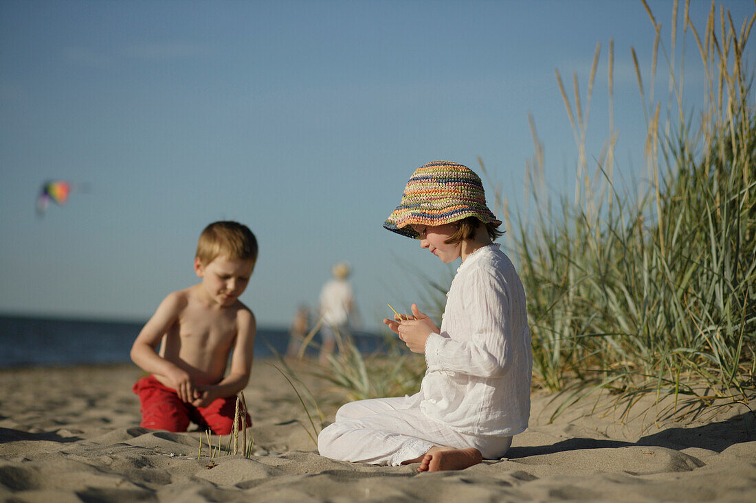 Mädchen und Junge sitzen am Ostseestrand und spielen, Travemünder Bucht, Schleswig-Holstein, Deutschland