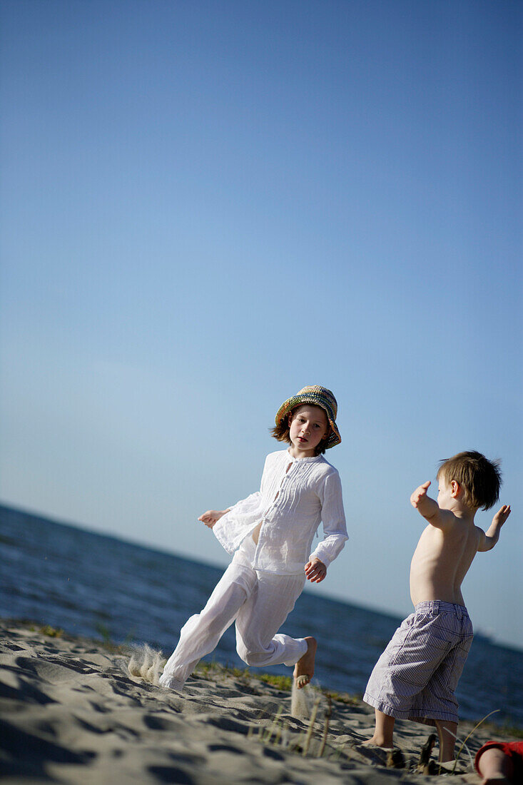 Girl running over Baltic Sea beach, boy blockading the way, Travemuende Bay, Schleswig-Holstein, Germany