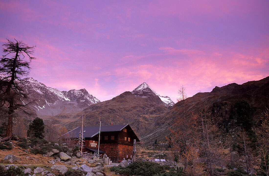 Lienzer hut in pink morning mood with larches in autumn colours, view to Debantgrat, Ralfspitz and Gloedis, Hochschober range, National Park Hohe Tauern, East Tyrol, Austria