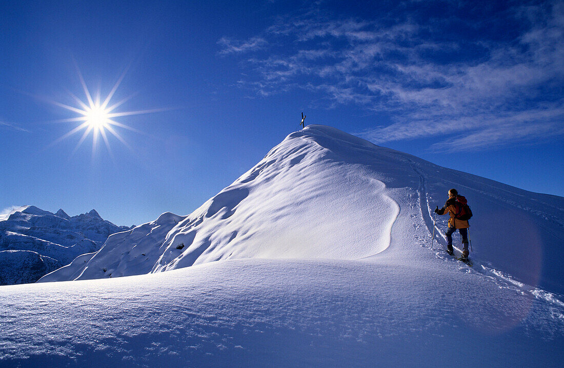 Mountaineerer with snowshoes ascending snow covered summit of Plassen, view to Dachstein, Dachstein range, Upper Austria, Austria