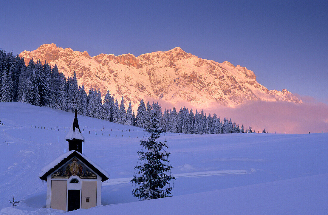 Verschneite Kapelle mit Hochkönig im Hintergrund bei Alpenglühen, Maria Alm, Salzburg, Österreich