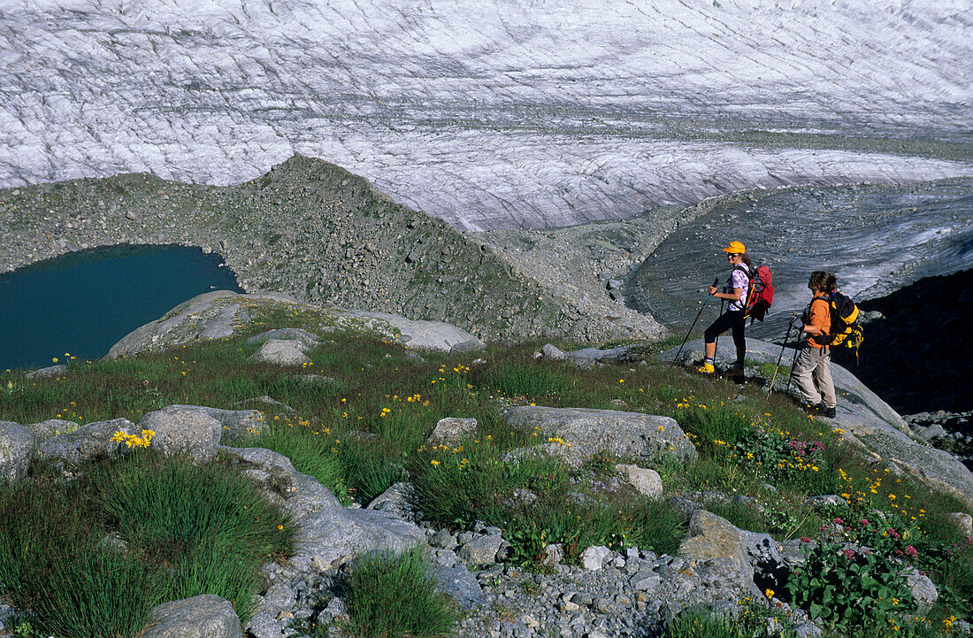 Two mountaineerers on a moraine of Isla Pers above a glacier lake and Morteratsch glacier, Bernina, Oberengadin, Grisons, Switzerland