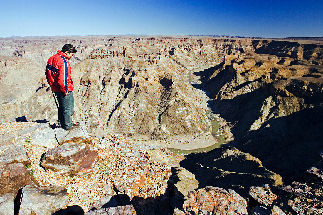 A young man looks down into the fish river canyon. Fish River Canyon Park, southern Namibia, Africa.
