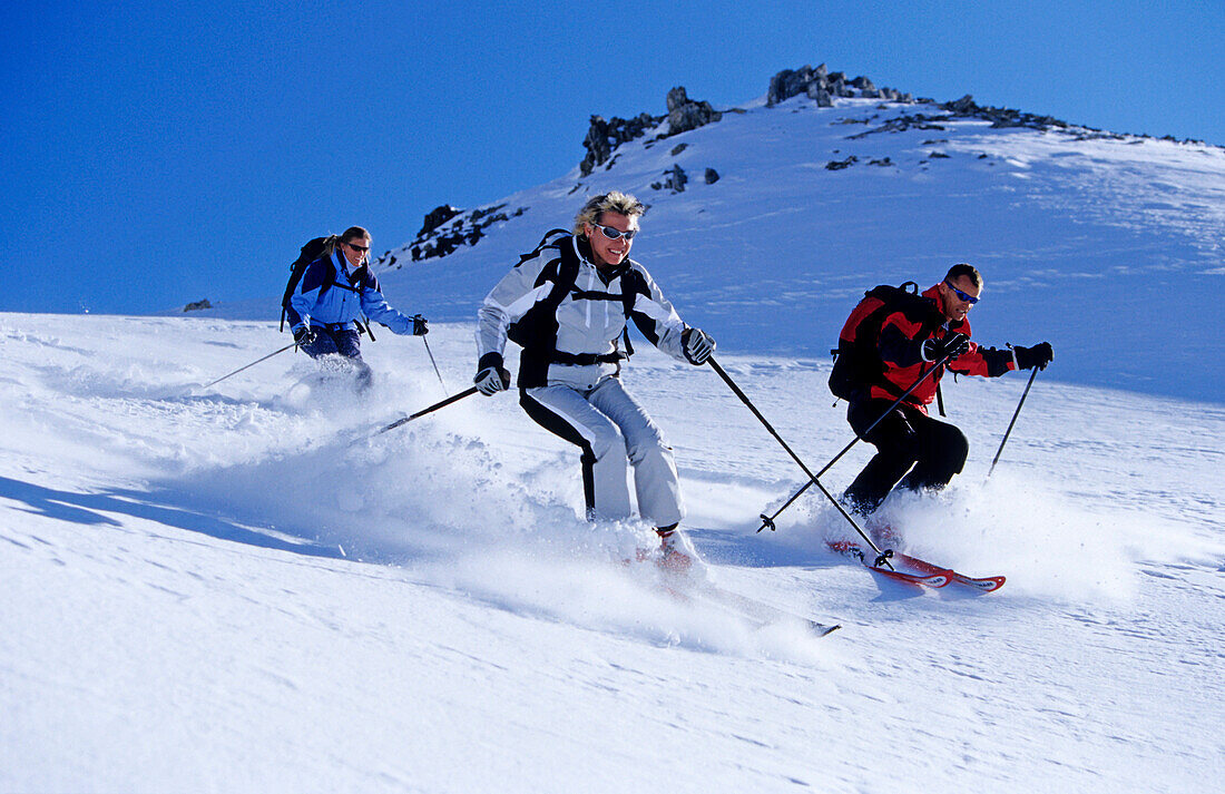 Drei junge Leute, zwei Frauen und ein Mann, fahren Tiefschnee im Skigebiet Parsenn, Davos, Klosters, Graubünden, Graubuenden, Schweiz, Alpen, Europa