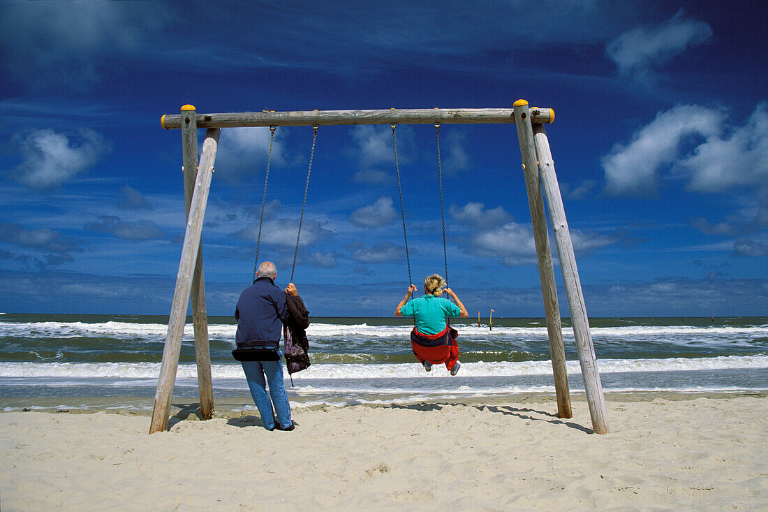 Elderly couple swinging on the beach, North Sea, Germany