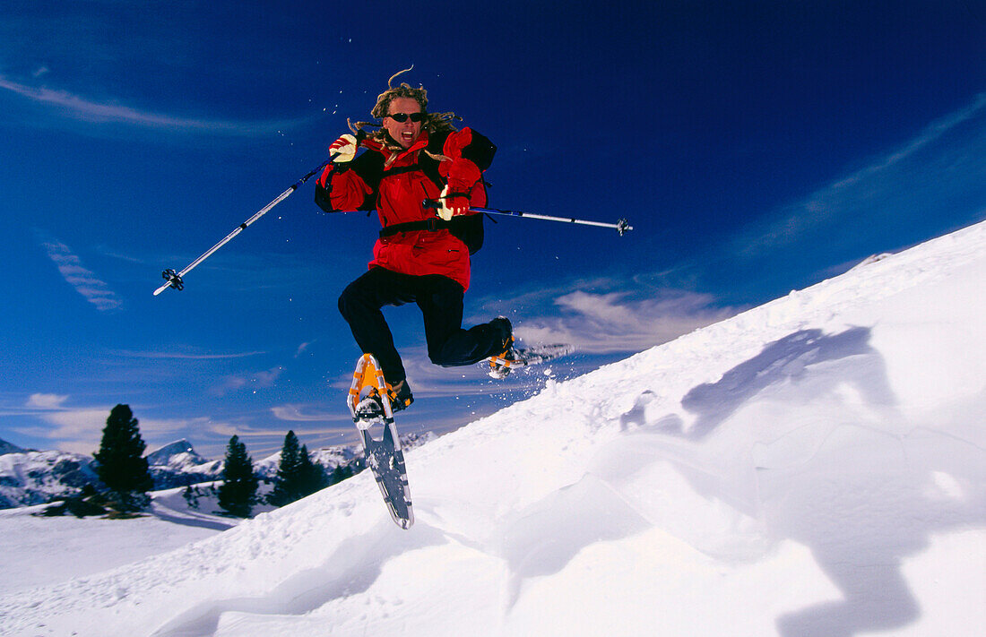 Mann springt in der Luft während einer Schneeschuhwanderung, Dolomiten, Italien