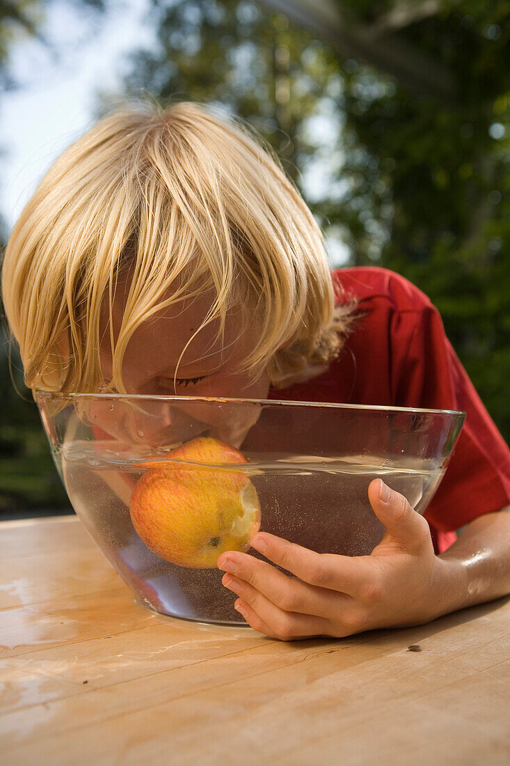 Junge isst einen Apfel in einer Schüssel mit Wasser, Kindergeburtstag