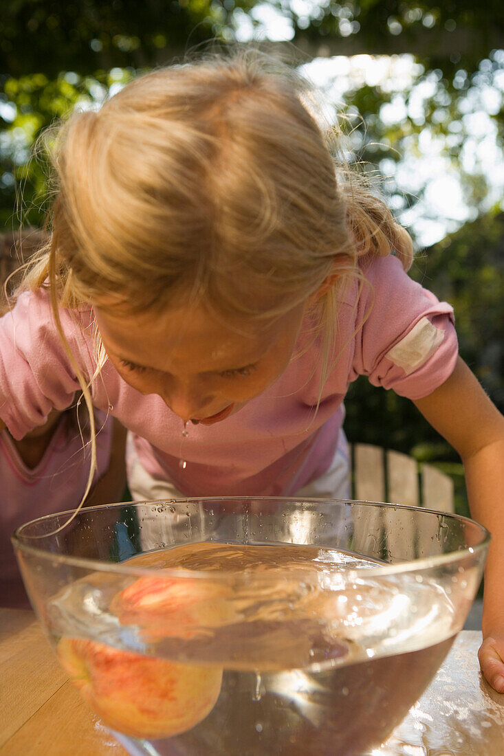 Mädchen beugt sich über eine Schüssel mit Wasser und einen Apfel, Kindergeburtstag
