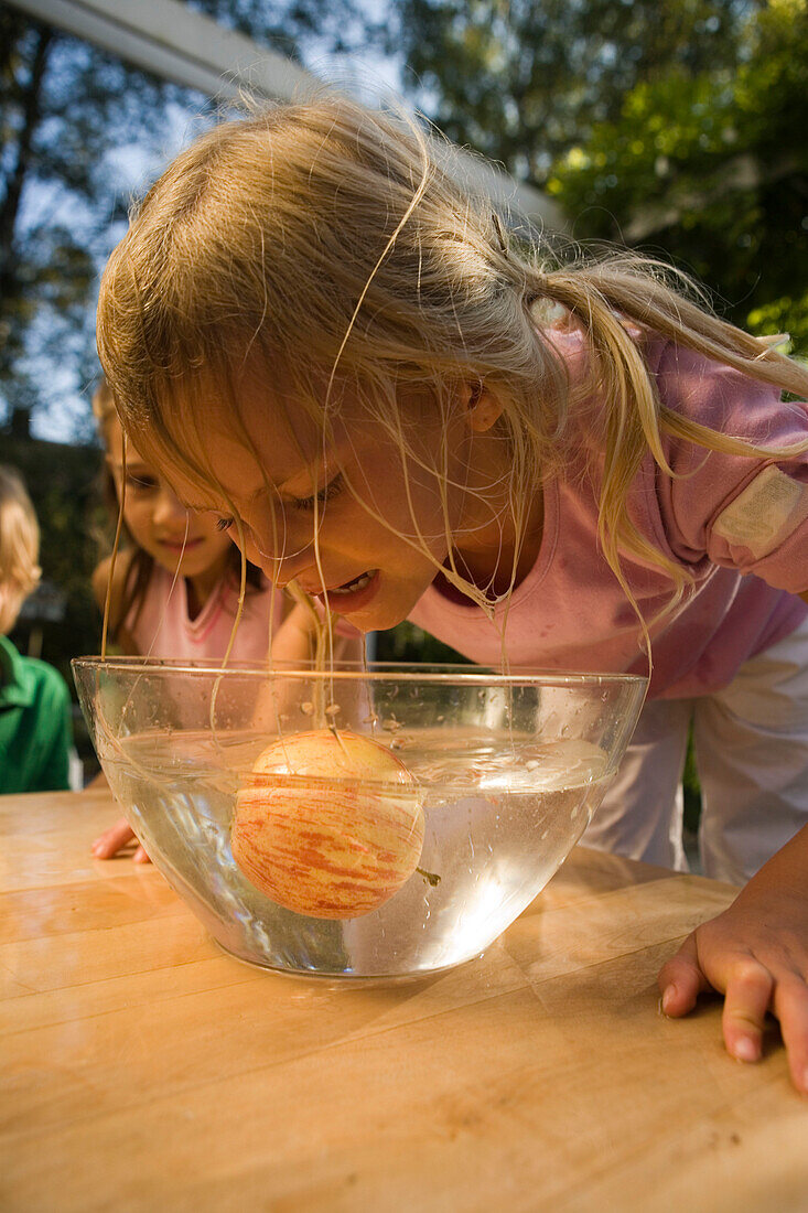 Nasses Mädchen beugt sich über eine Schüssel mit Wasser und einem Apfel, Kindergeburtstag