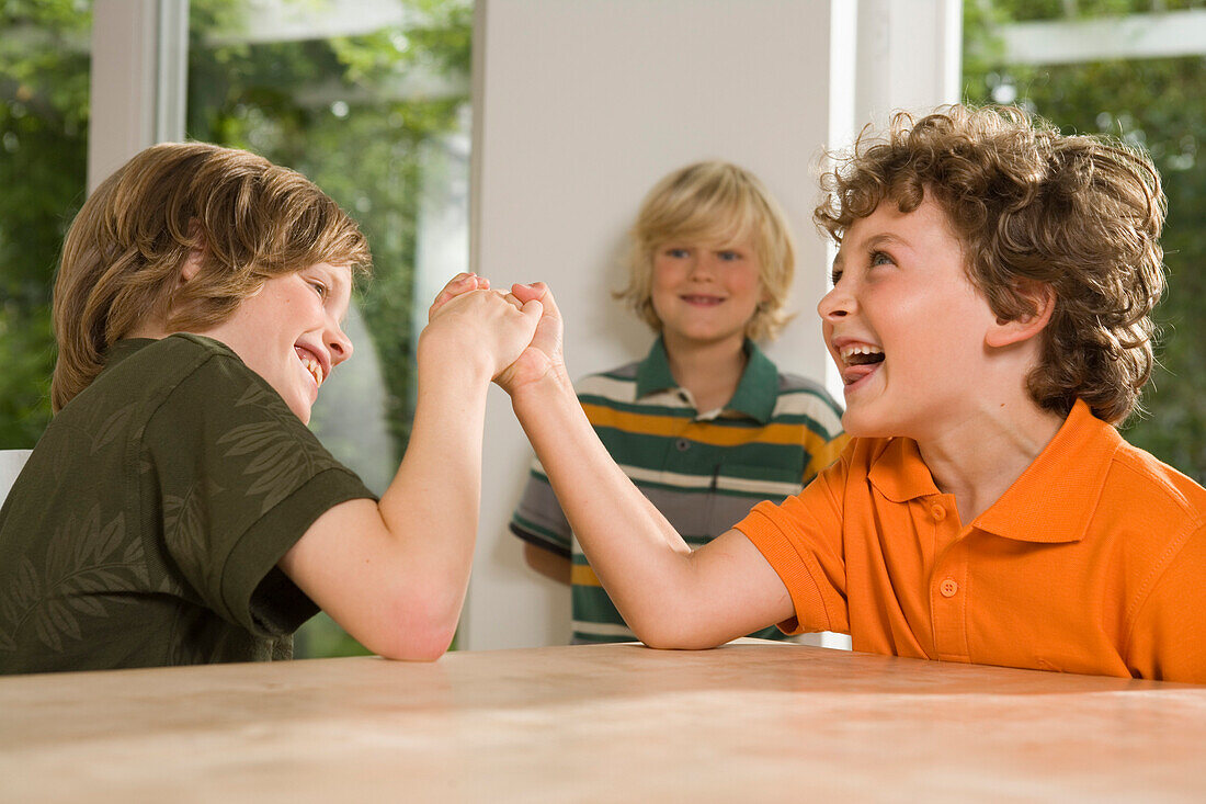 Zwei Jungen beim Armdrücken, anderer Junge steht im Hintergrund, Kindergeburtstag
