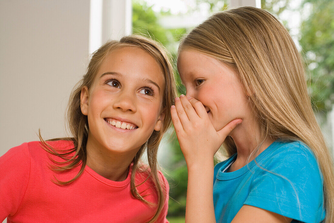 Mädchen flüstert Freundin etwas ins Ohr, Kindergeburtstag