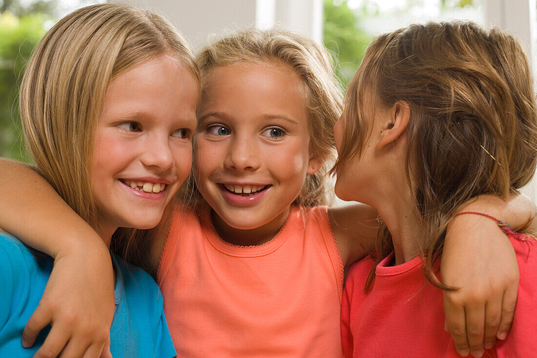 Three girls standing side by side and whispering, children's birthday party