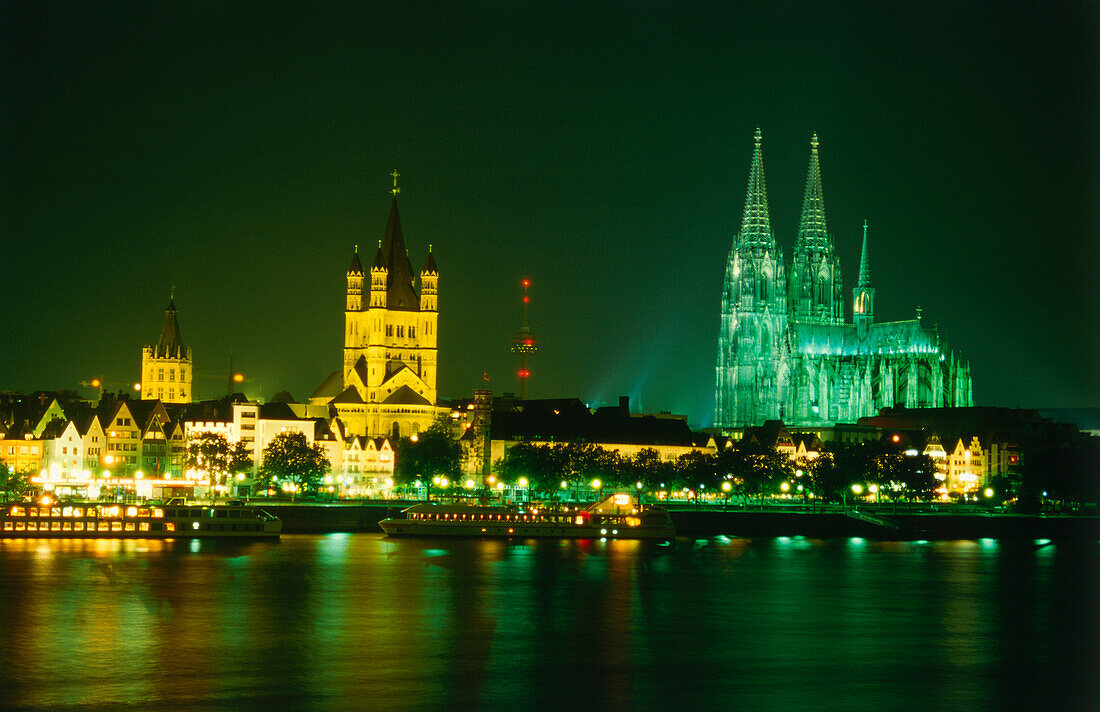 View over River Rhine to illuminated city hall, Great St. Martin Church and Cologne Cathedral at night, Cologne, North Rhine-Westphalia, Germany