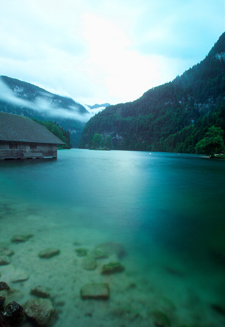 View of Koenigssee with wooden hous and mountains in background in the evening, Berchtesgaden National Park, Schoenau, Bavaria, Germany