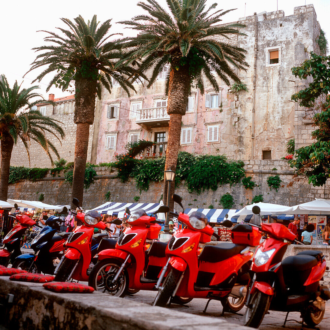 Red scooter parking in a row near a market, old stone building in background, Korcula, Dalmatia, Croatia