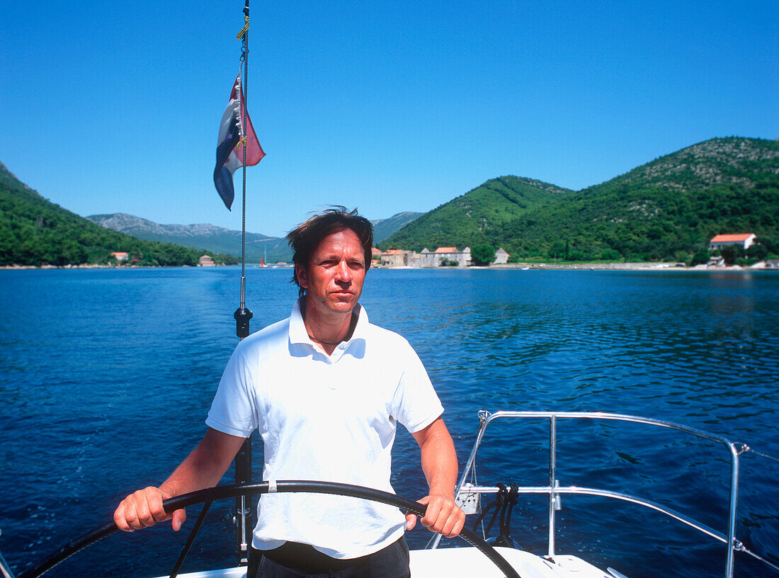 Mann am Steuerad eines Segelboots auf der Adria, Dalmatien, Kroatien