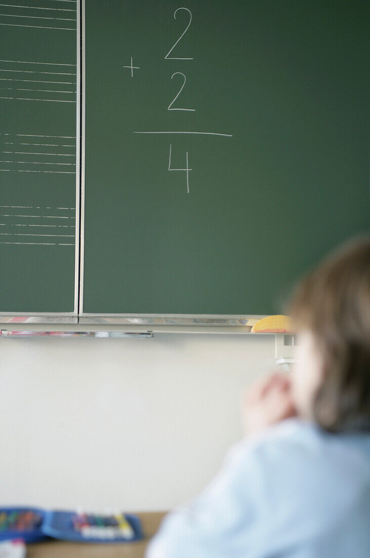 Boy sitting in classroom, arithmetic problem at blackboard