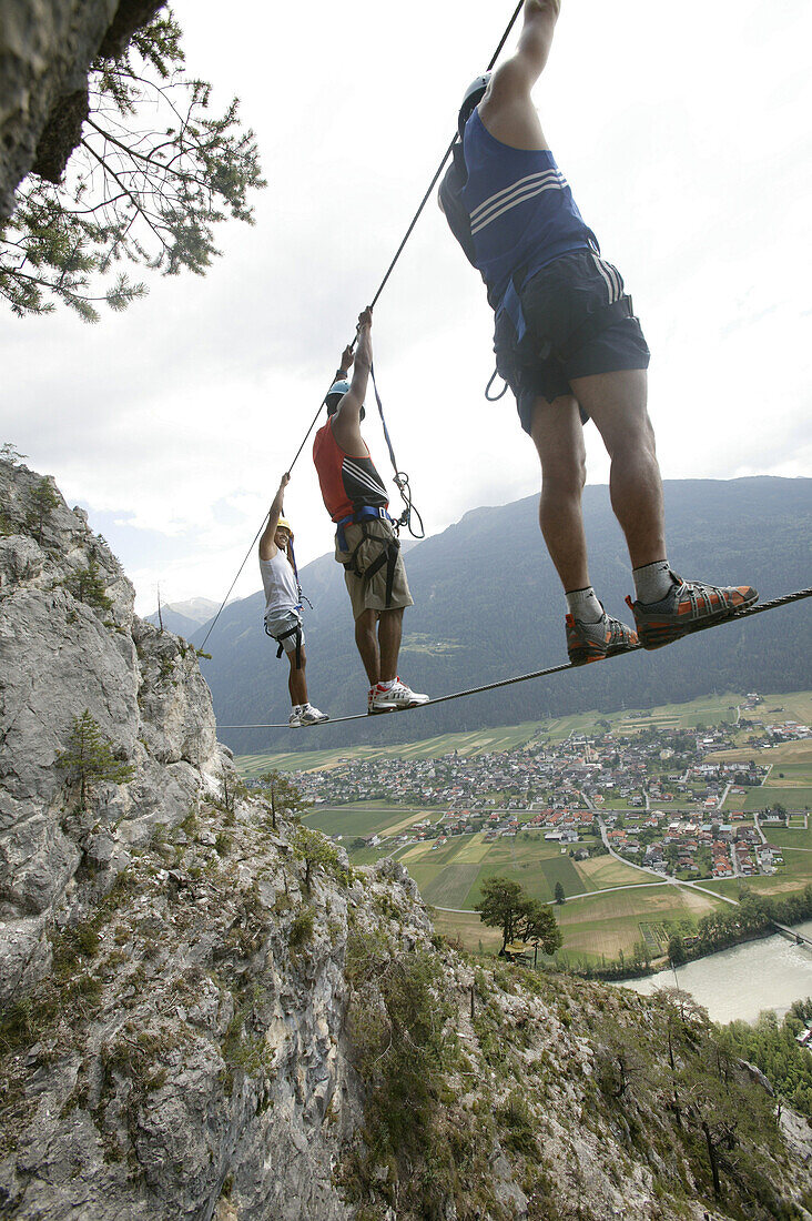 Three men climbing on a rope bridge at Crazy Eddy in Silz, Haiming in the background, Tyrol, Austria
