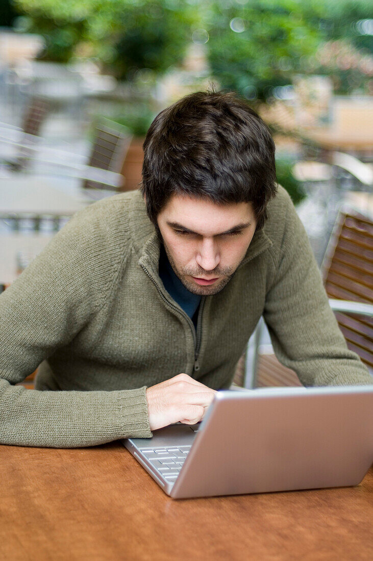 Junger Mann sitzt in einem Straßencafe und arbeitet an einem Laptop