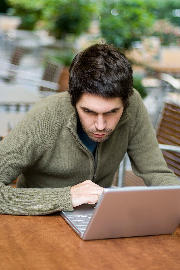 Young man sitting in a pavement cafe using a laptop