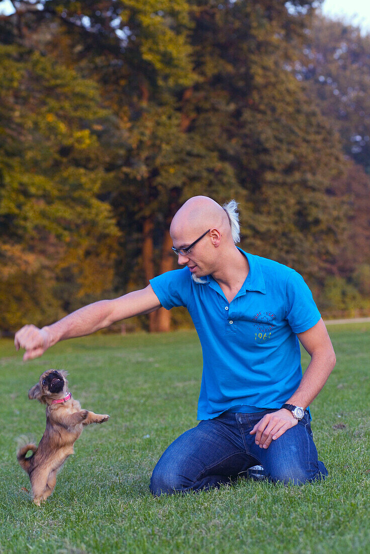 Mann spielt mit Hund im Englischen Garten, Schwabing, München, Deutschland