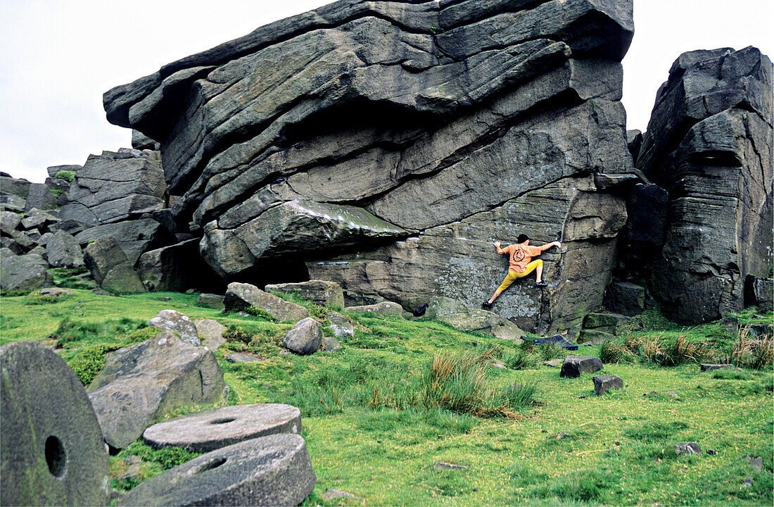 Bouldern im Peakdistrict nahe Sheffield, UK. Ein Mann bouldert, klettert an einem Sandsteinfelsen, im Vordergrund Mühlesteine. England, Europa, MR
