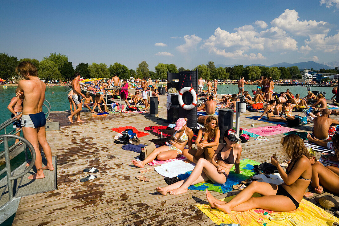 Young people sunbathing on landing stage at Strandbad Klagenfurt, Lake Wörthersee (biggest lake of Carinthia), Klagenfurt, Carinthia, Austria