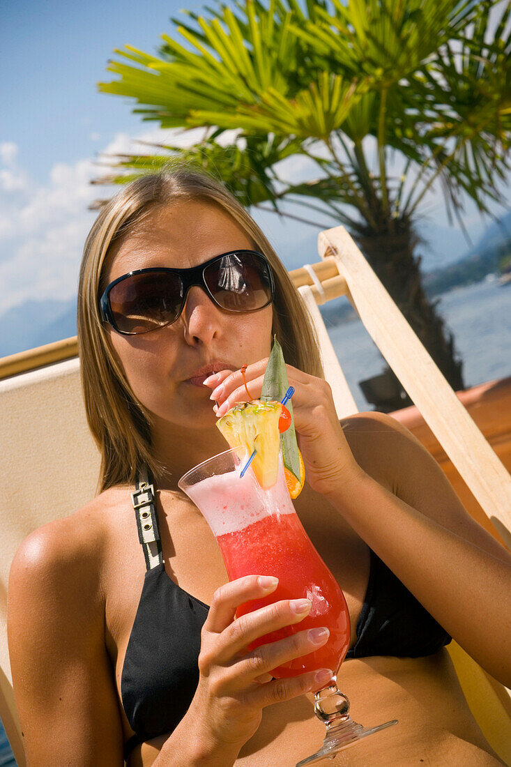 Young woman wearing a bikini drinking a fruit cocktail, Millstaetter See, the deepest lake in Carinthia, Millstatt, Carinthia, Austria