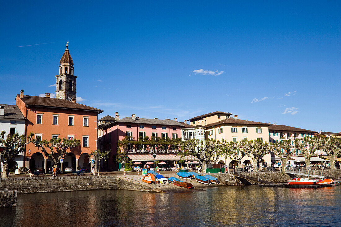 View over Lake Maggiore to harbour promenade with spire of church Santi Pietro Paolo in background, Ascona, Ticino, Switzerland