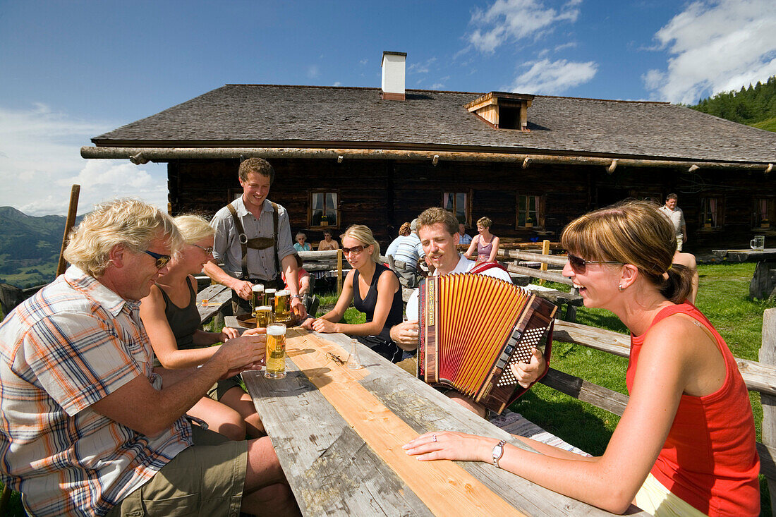 Mann serviert Bier und Musiker spielt Akkordeon, Bichlalm 1731 m, Grossarltal, Salzburg, Österreich