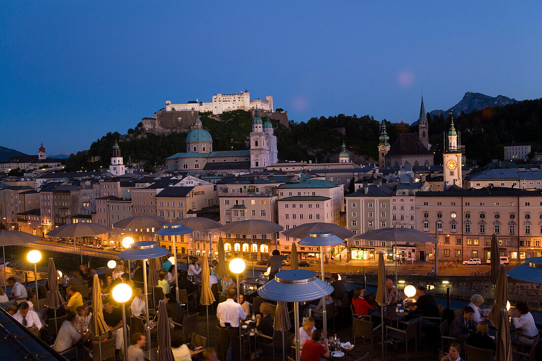 View over illuminated roof deck of restaurant Hotel Stein to old town with Salzburg Cathedral, St. Peter's Archabbey, Franciscan Church, City Hall Tower and  Hohensalzburg Fortress, largest, fully-preserved fortress in central Europe, in the evening, Salz