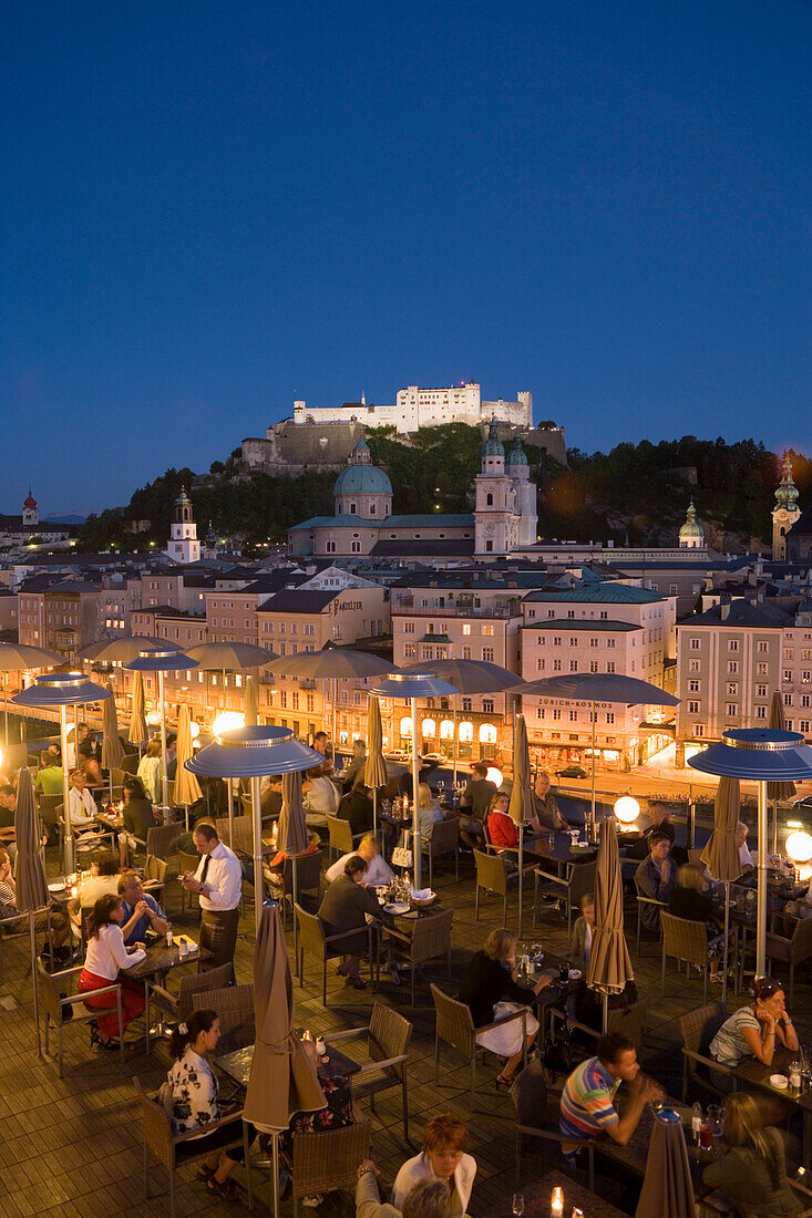 View over the illuminated roof terrace of restaurant Hotel Stein in the evening, to old town with Salzburg Cathedral and Hohensalzburg Fortress the largest fully preserved fortress in central Europe, Salzburg, Salzburg, Austria