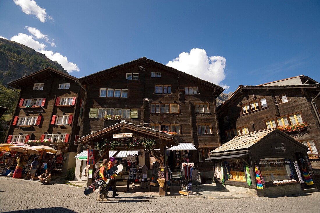 Two snowboarder passing a souvenir shop at Bahnhofplatz, Zermatt village, Zermatt, Valais, Switzerland