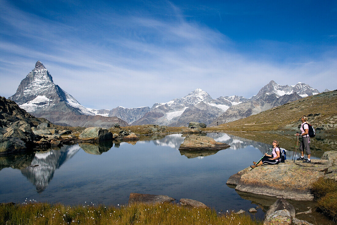 Two female hikers looking at the reflection of the east face, Hoernligrat, of the Matterhorn, 4478 m, in Riffelsee, Zermatt, Valais, Switzerland