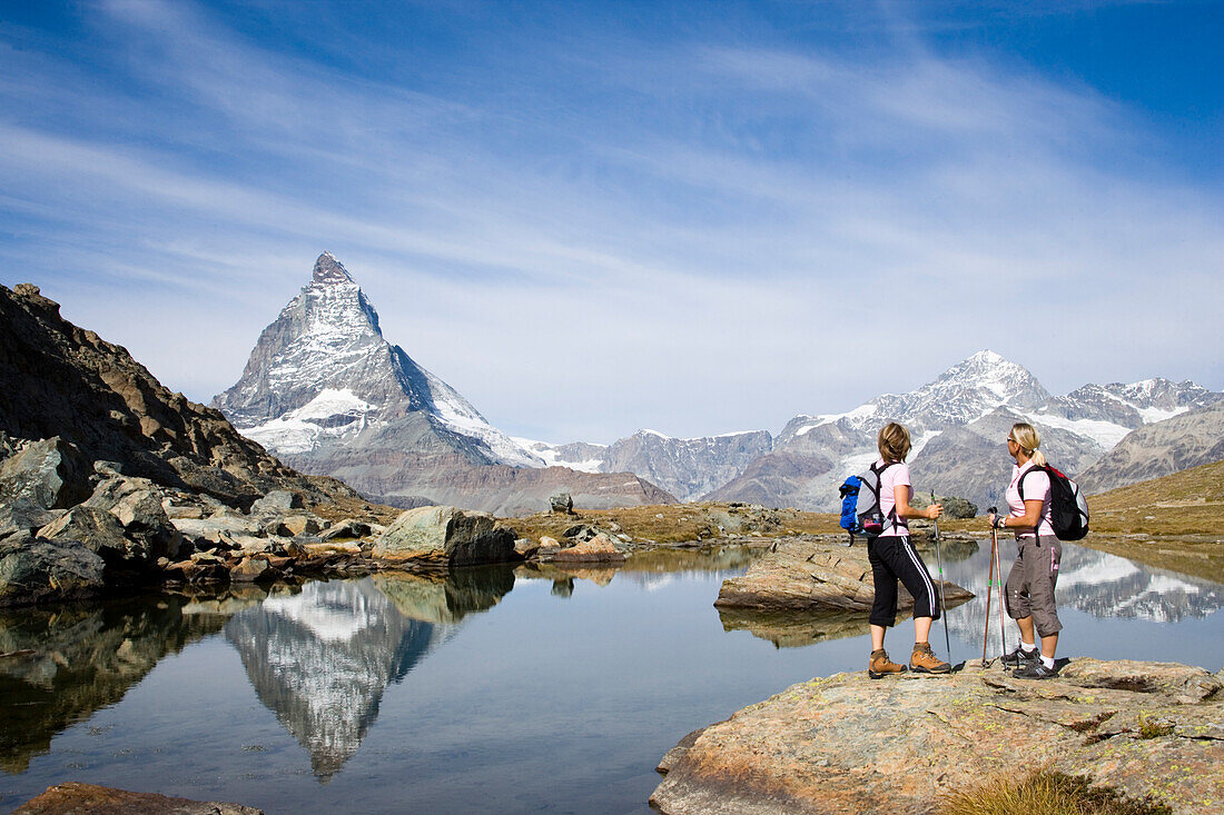Two female hikers looking at the reflection of the east face, Hoernligrat, of the Matterhorn, 4478 m, in Riffelsee, Zermatt, Valais, Switzerland