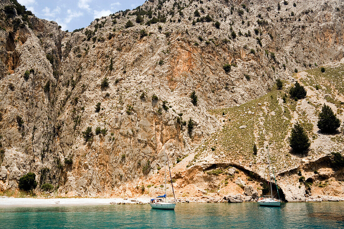 Two sailing boats anchoring near beach in Sisalona Bay, rock face in background, Symi Island, Pedi, Greece