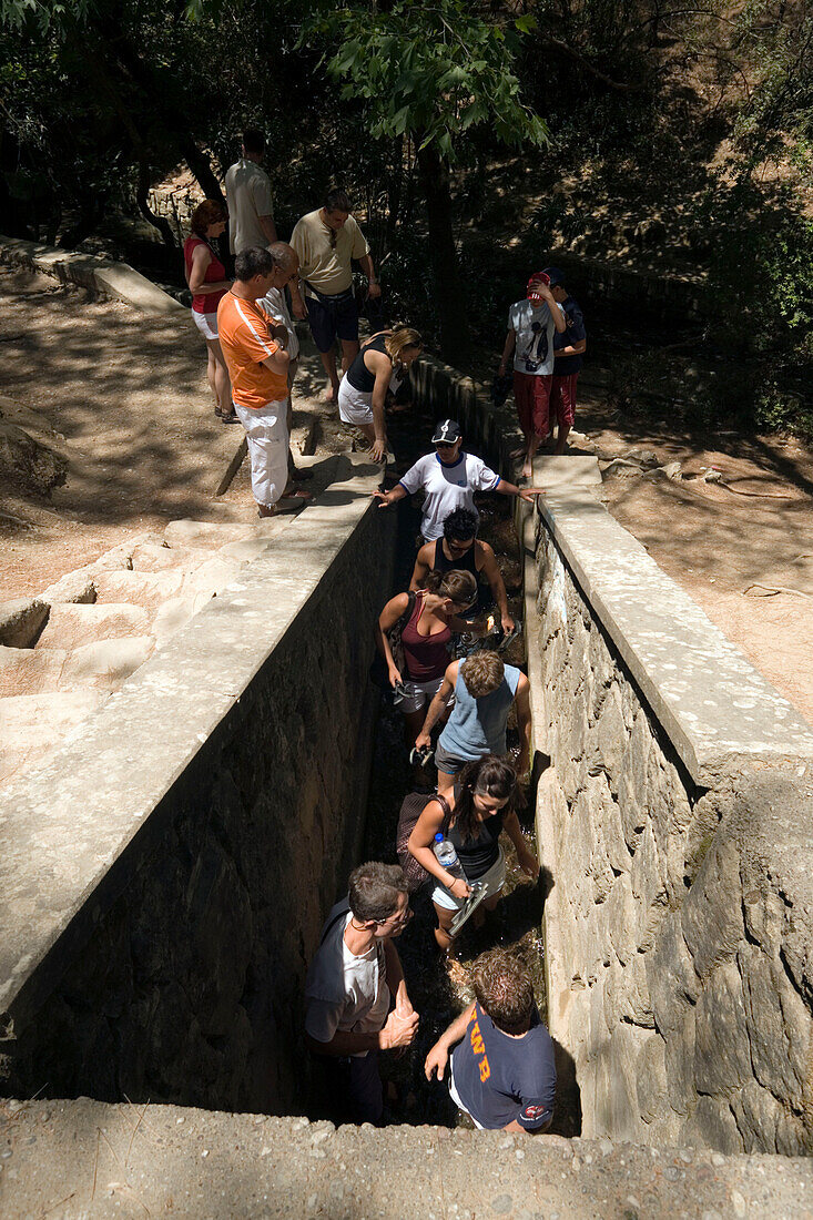 Group of tourists walking through the dark tunnel with ankle high water to reservoir, Epta Piges (Valley of the seven springs), near Colymbia, Rhodes, Greece