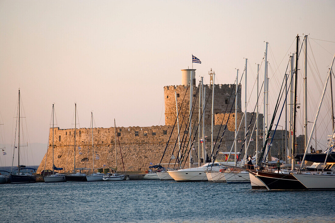 View along anchoring ships at mole with fortress tower Agios Nikolaos in background, Mandraki harbour (translated literally: fold), Rhodes Town, Rhodes, Greece