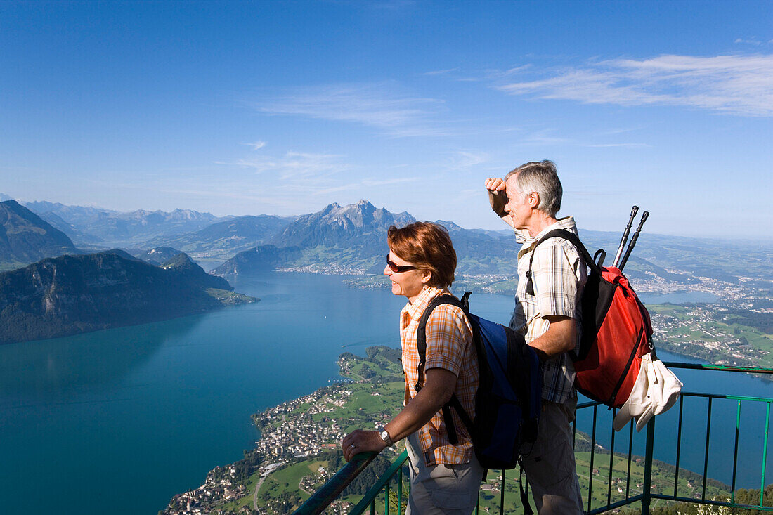 Mature adult couple at Kanzli vantage point on Mount Rigi (1797 m, Queen of the Mountains) looking over Lake Lucerne and Weggis, Mount Bürgenstock and Mount Pilatus (2132 M) in the background, Rigi Kaltbad, Canton of Schwyz, Switzerland