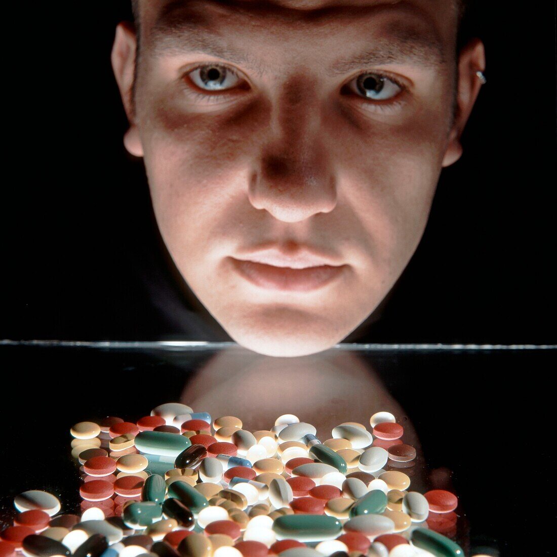 Male face with pills in foreground, Studio shot