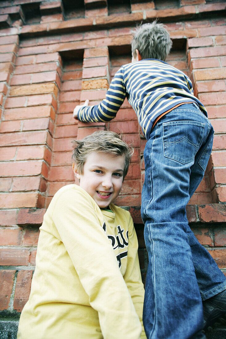 Boy giving friend a bunk-up over a wall