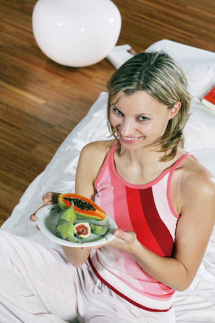Young woman relaxing in bed with a plate of exotic fruits