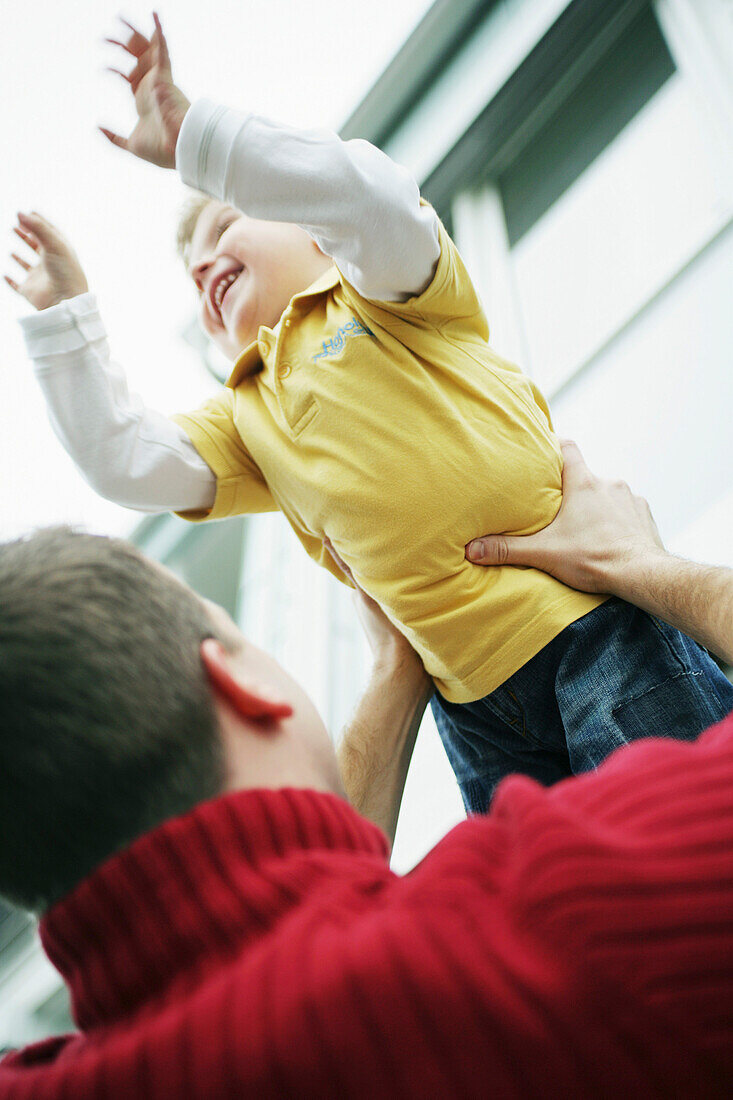 Father lifts son in the air, laughing