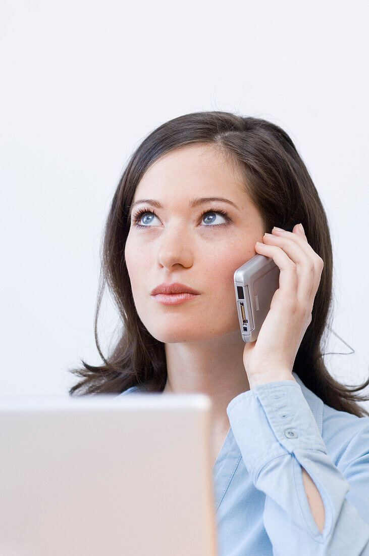 Junge Frau am Laptop telefoniert mit einem Handy