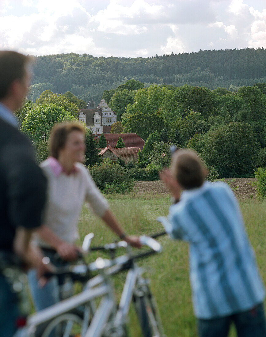 Fahrradausflug, sportliche Familie mit Sohn, mit Fahrrädern auf einer Wiese, im Hintergrund das Schloßhotel Münchhausen, bei Hameln, Weserbergland, Niedersachsen, Deutschland