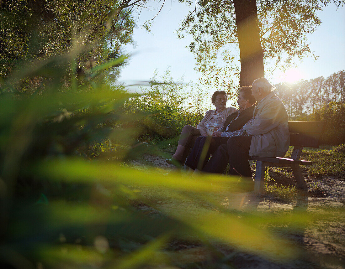 Senioren sitzen auf einer Bank am Flußufer des Inn, Abendsonne, bei Bad Füssing, Bayern, Deutschland